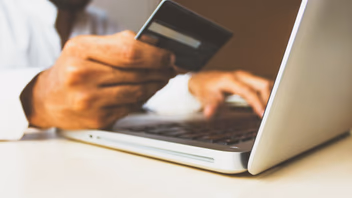 Homme tenant une carte bancaire devant son ordinateur portable pour régler un achat en ligne
