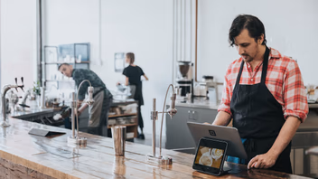 Commerçant derrière le comptoir de son café, devant une caisse enregistreuse sur tablette
