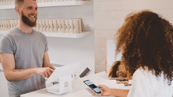 Cliente payant avec son smartphone au comptoir d’une boutique, face au vendeur
