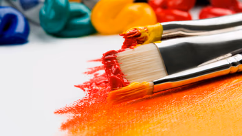 Pinceaux chargés de peinture rouge et jaune posés sur une toile aux couleurs vives