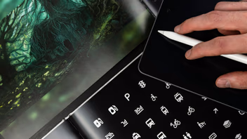 Main d’un designer travaillant au stylet sur une tablette graphique, à côté de planches de pictogrammes